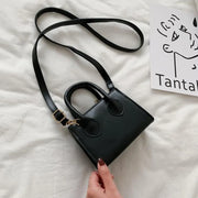 Petit sac à main cuir noir élégant avec bandoulière réglable sur fond clair.