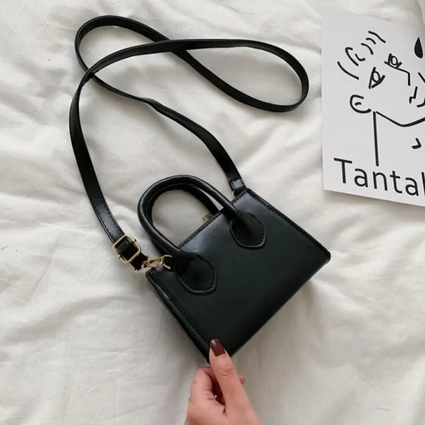 Petit sac à main cuir noir élégant avec bandoulière réglable sur fond clair.